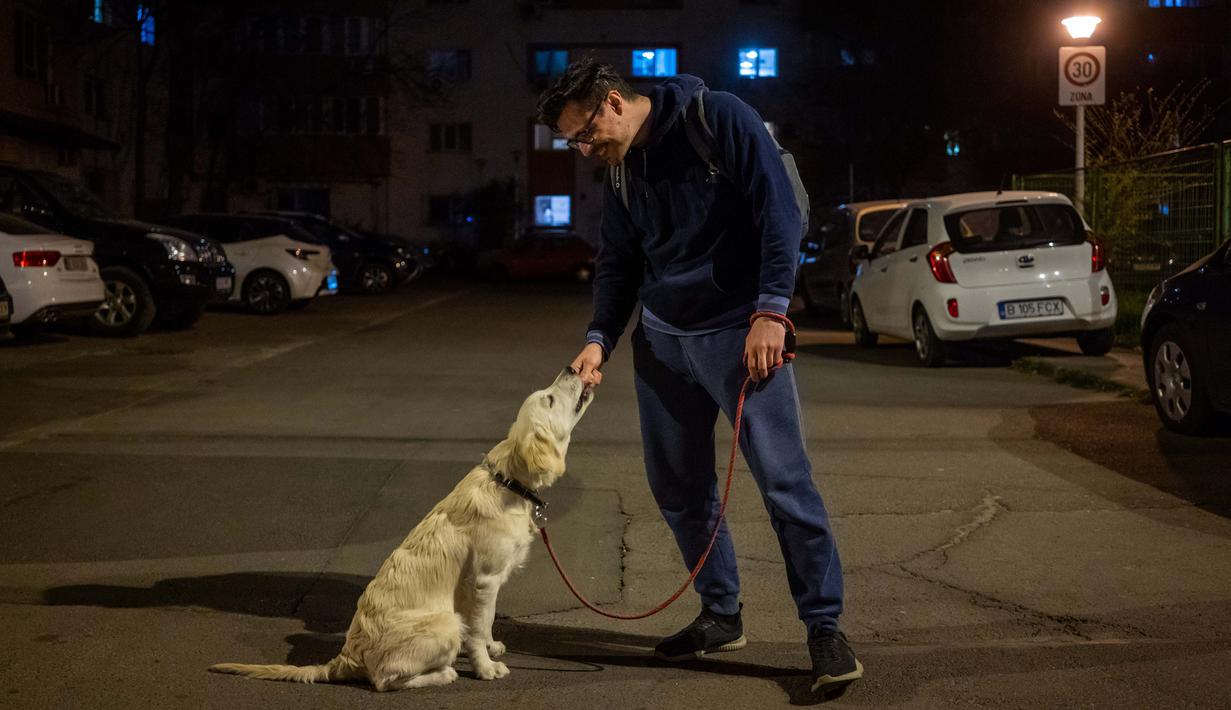 Iulian Barbulescu (34) berpose dengan anjingnya Jesse  (5 bulan) di Bucharest (28/3/2020). Undang-undang militer, yang disahkan pemerintah Rumania untuk mengurangi penyebaran virus corona, menyatakan berjalan bersama anjing adalah salah satu  kegiatan yang masih diizinkan. (AFP/Andrei Pungovschi)