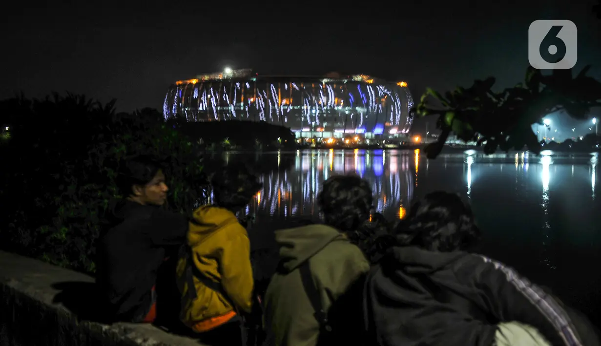 Warga menyaksikan warna-warni lampu Jakarta International Stadium (JIS) dari Waduk Cincin, Papanggo, Jakarta Utara, Rabu (16/3/2022). PT Jakarta Propertindo (Jakpro) menargetkan pembangunan JIS rampung dan siap dibuka pada April 2022. (merdeka.com/Iqbal S. Nugroho)