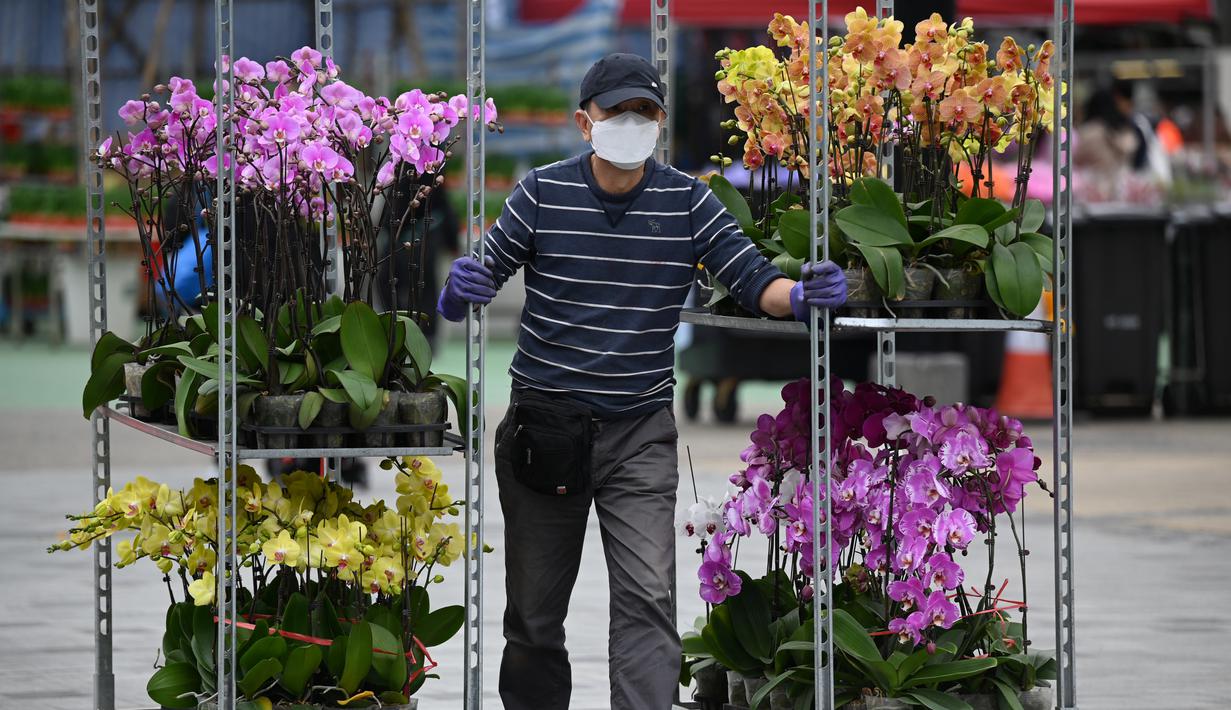 <p>Seorang pedagang membawa bunga yang akan dijual pada hari pembukaan pasar bunga di Hong Kong (16/1/2023). Menjelang Tahun Baru Imlek yang menandai tahun Kelinci pasar bunga di Hong Kong mulai ramai di kunjungi pengunjung. (AFP/Peter Parks)</p>