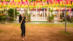 Seorang perempuan menggantung lampion di Wat Phra That Hariphunchai, Lamphun, Thailand, 1 November 2020. Sekitar 100.000 lampion digantung di Wat Phra That Hariphunchai sebagai bagian dari perayaan festival tradisional Yi Peng. (Xinhua/Zhang Keren)
