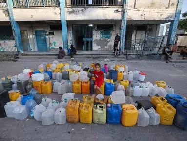 Seorang anak perempuan Palestina duduk di atas jerigen kosong sambil menunggu truk distribusi air di sekolah Abou Helou yang dikelola UNRWA, tempat para pengungsi perempuan berlindung di kamp pengungsi Bureij di Jalur Gaza tengah, pada 17 Juli 2025. (Eyad BABA/AFP)