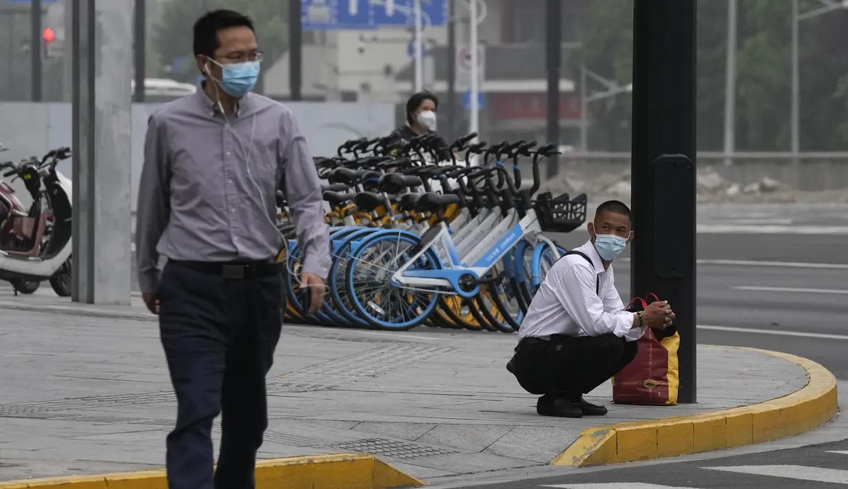 <p>Seorang pria bermasker jongkok saat menunggu untuk menyeberang jalan di Shanghai (2/6/2022). Lalu lintas, pejalan kaki dan pelari muncul kembali di jalan-jalan Shanghai ketika kota terbesar di China mulai kembali normal di tengah pelonggaran penguncian COVID-19 dua bulan yang ketat atas penerapannya. (AP Photo/Ng Han Guan)</p>