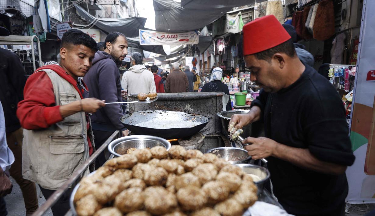 Meski berada dalam kondisi sulit dan harga barang yang melonjak tinggi, Pasar Al-Zawiya tetap ramai dikunjungi. Tampak dalam foto, pedagang kaki lima Palestina membuat falafel di pasar Zawiya Kota Gaza pada Rabu 18 Februari 2026. (Omar AL-QATTAA/AFP)