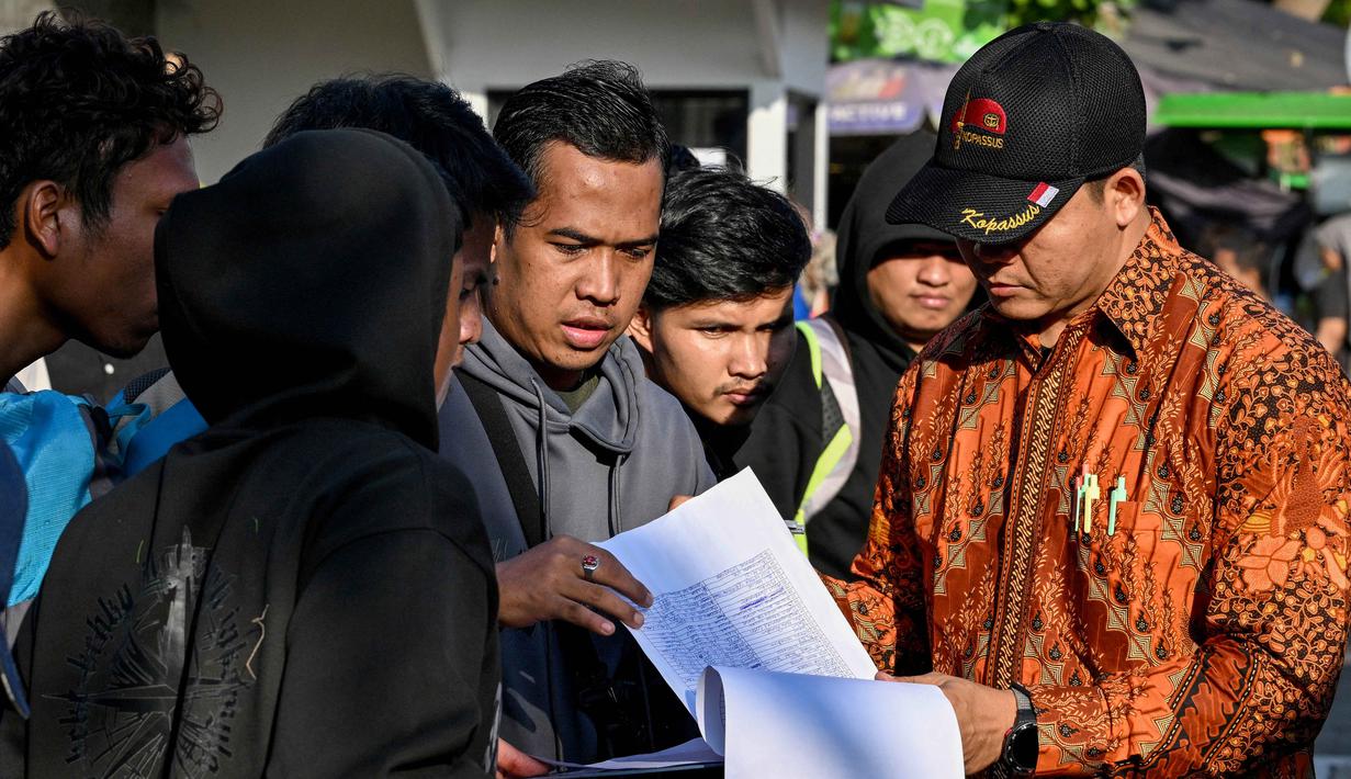 Sementara itu, terdapat empat WNI yang telah kembali ke Indonesia secara mandiri pada Selasa pagi (20/1/2026). Tampak dalam foto, orang-orang memeriksa nama mereka di daftar di depan Kedutaan Besar Republik Indonesia (KBRI) di Phnom Penh, Kamboja, pada Rabu 21 Januari 2026. (TANG CHHIN Sothy/AFP)