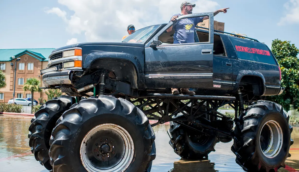 Warga menurunkan barangnya truk raksasa saat kembali ke rumah mereka di Port Arthur, Texas, AS (1/9). Truk raksasa ini menjadi salah satu kendaraan yang diandalkan usai Badai Harley menghantam Texas. (AFP Photo/Emily Kask)