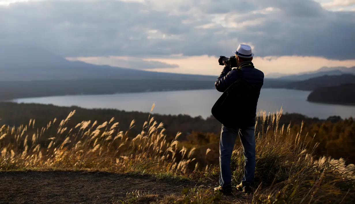 Turis mengambil foto Gunung Fuji di samping danau Yamanaka di desa Yamanakako, Prefektur Yamanashi, Jepang (1/11). Gunung Fuji dikelilingi oleh tiga kota yaitu Gotemba (timur), Fuji-Yoshida (utara) dan Fujinomiya (barat daya). (AFP Photo/Behrouz Mehri)