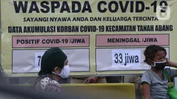 Warga duduk di depan tanda peringatan bahaya COVID-19 di sekitar Pasar Blok A Tanah Abang, Jakarta, Selasa (1/9/2020). Guna meningkatkan kewaspadaan warga, muspida kecamatan Tanah Abang memajang peti mati dilengkapi data jumlah korban COVID-19 di wilayah tersebut. (Liputan6.comHelmi Fithriansyah)