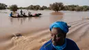 Orang-orang membawa barang-barang di atas kereta dorong di atas air banjir yang mengalir di jalan utama Odobere pada tanggal 22 Oktober 2024. (GUY PETERSON/AFP)