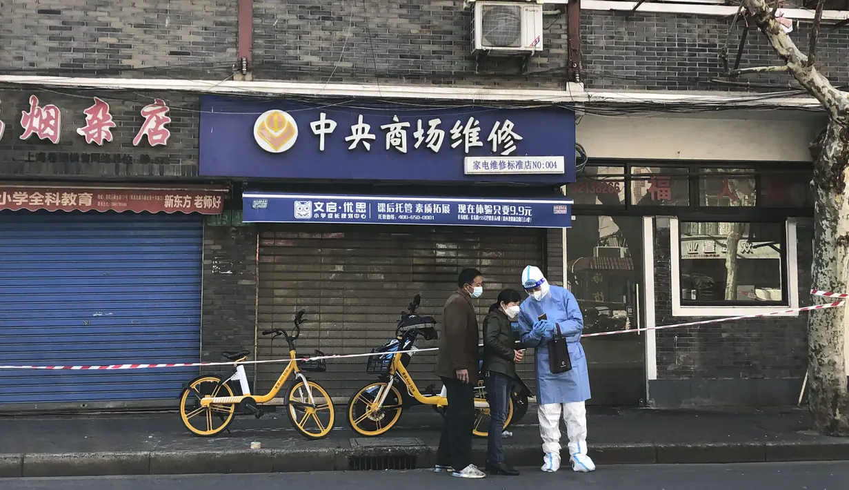 Seorang pekerja dengan alat pelindung mengobrol dengan penduduk di luar toko yang tutup di distrik Jingan, Shanghai barat (4/4/2022). China telah mengirim lebih dari 10.000 petugas kesehatan dari seluruh negeri ke Shanghai, termasuk 2.000 staf medis militer. (AP Photo/Chen Si)