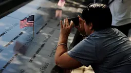 Seorang wanita memotret bendera nasional yang diletakkan di situs nama-nama para korban peristiwa serangan 11 September 2001 lalu di National September 11 Memorial and Museum at the World Trade Center, New York, Sabtu (10/9). (REUTERS/Mark Kauzlarich)