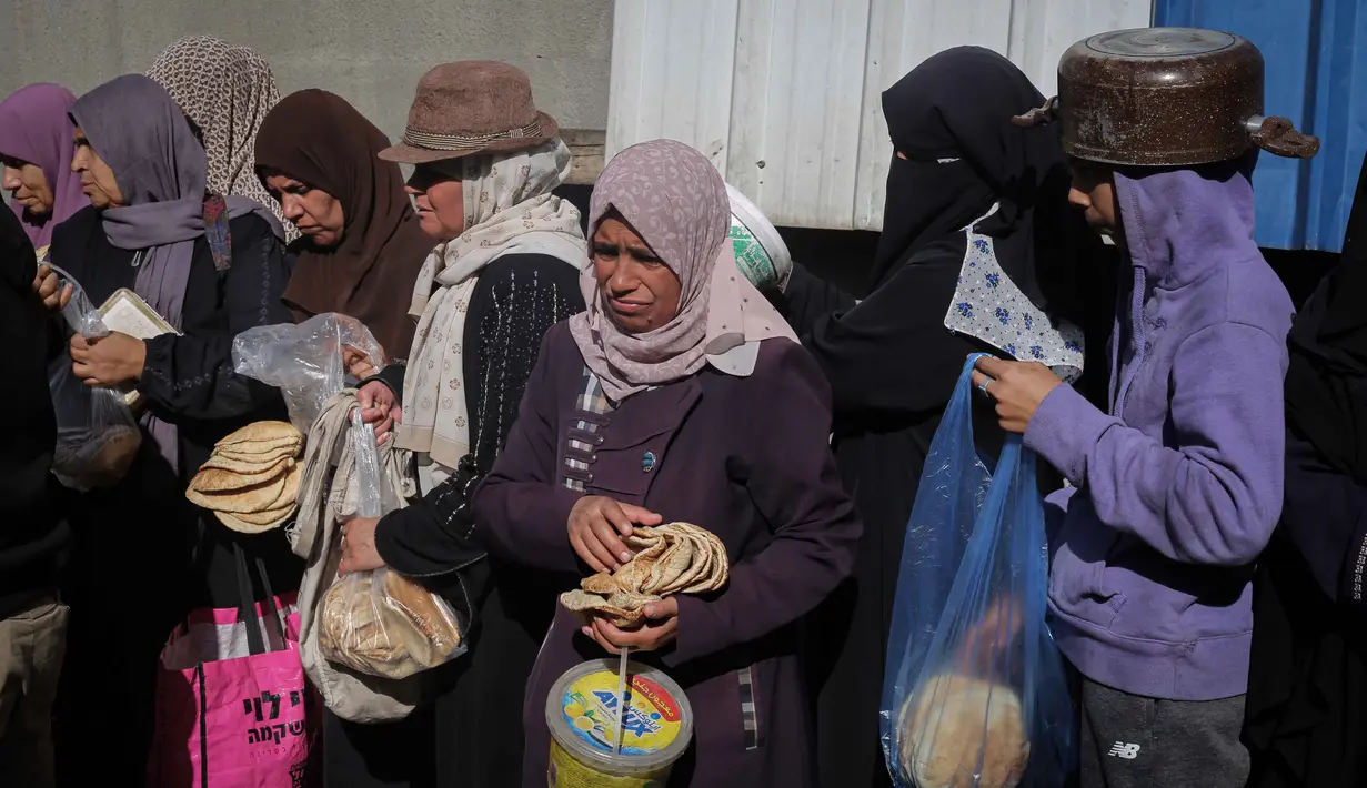 Penghalangan akses dan hambatan penyaluran bantuan ini jelas menghambat proses pemulihan situasi dan kondisi di Gaza. Tampak dalam foto, warga Palestina yang terlantar, anak-anak, dan dewasa, menunggu makanan di sebuah tempat penampungan yang telah dihuni keluarga-keluarga di Nuseirat, pusat Jalur Gaza, pada 23 November 2025. (EYAD BABA/AFP)