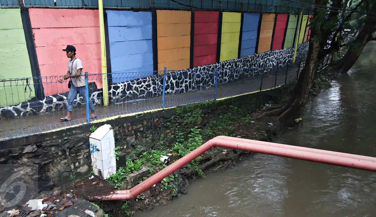 Warga melintas dekat tembok warna-warni di Kampung Penas Tanggul, Cipinang Besar Selatan, Jakarta, Kamis (23/3). Kampung warna-warni tanpa rokok itu dibuat warga sebagai bentuk upaya perlindungan bagi perempuan dan anak. (Liputan6.com/Immanuel Antonius)
