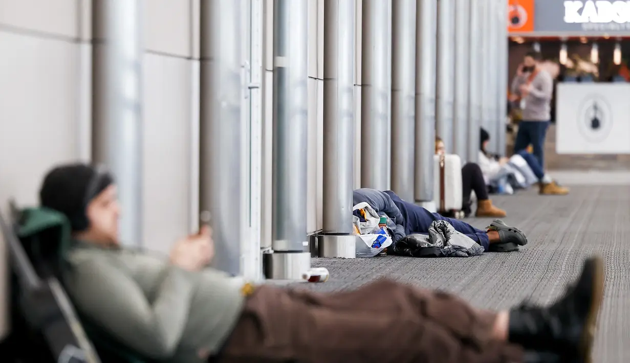 Pelancong menemukan ruang di lantai untuk menunggu di Bandara Internasional Denver setelah banyak penerbangan dibatalkan dan ditunda selama badai musim dingin di Denver, Colorado, Rabu (22/2/2023). Lebih dari 1.000 penerbangan telah dibatalkan di seluruh Amerika Serikat (AS) karena badai berdampak pada perjalanan di seluruh negeri. (Michael Ciaglo/Getty Images/AFP)