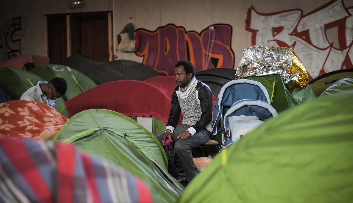 Para lelaki duduk di dekat tenda di sebuah gimnasium yang ditempati oleh para migran di lycee Jeanne-Bernard di Saint-Herblain, di luar Nantes, barat Prancis (28/3). Sekitar 250 imigran saat ini tinggal di tempat tersebut. (AFP Photo/Loic Venance)