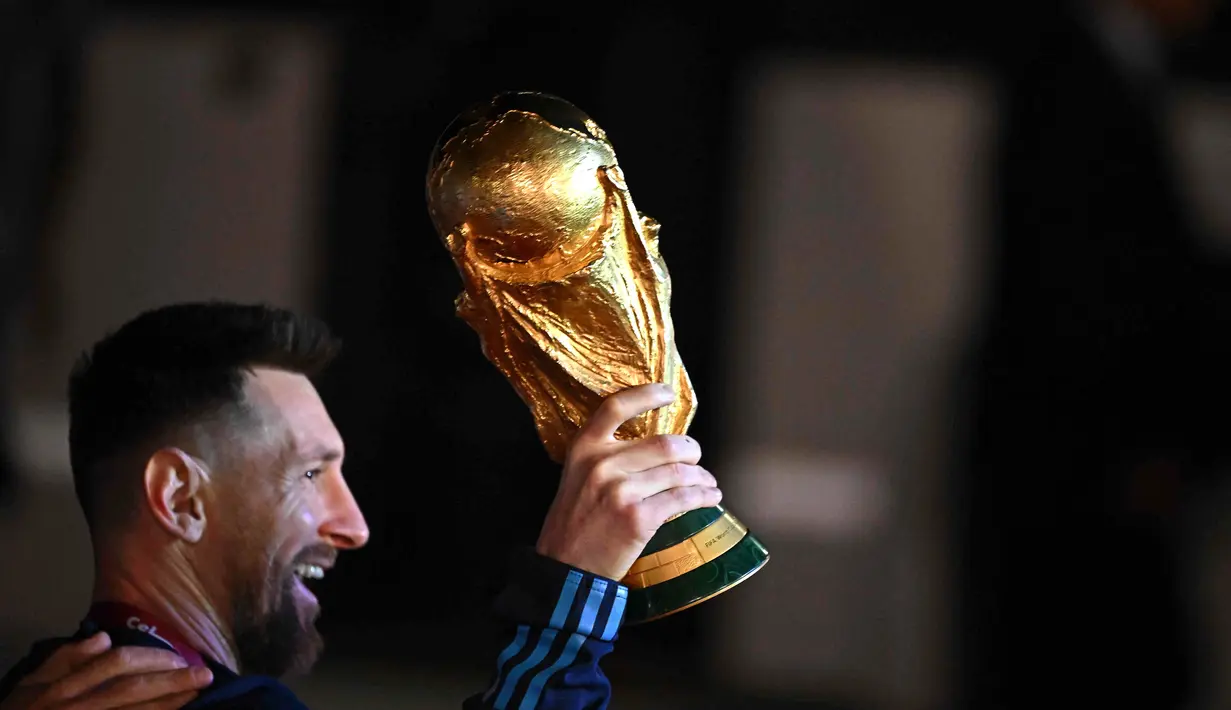 Kapten Argentina Lionel Messi (kiri) memegang Trofi Piala Dunia 2022 setibanya di Bandara Internasional Ezeiza di Ezeiza, provinsi Buenos Aires, Argentina (20/12/2022). Trofi Piala Dunia pertama yang dimenangi Argentina dicapai pada 1978. Argentina tampil sebagai juara di kandang sendiri dengan kemenangan atas Belanda 3-1. (AFP/Luis Robayo)