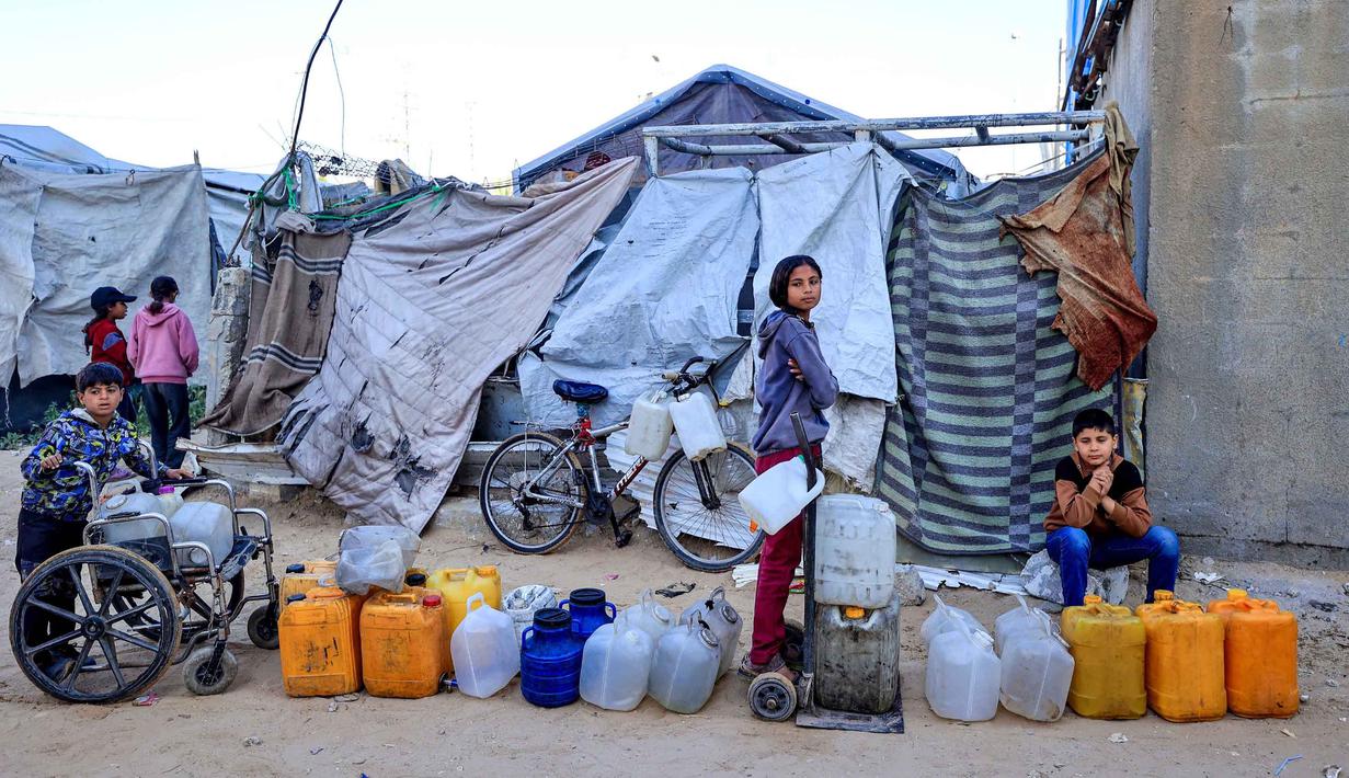 Rusak atau hancurnya sekitar 90 persen infrastruktur air dan sanitasi di Gaza juga menjadi penanda situasi krisis kemanusiaan yang ekstrem. Tampak dalam foto, anak-anak menunggu untuk mengisi wadah dengan air di kamp pengungsi Palestina, Nuseirat, Jalur Gaza Tengah pada Kamis 7 Mei 2026. (Eyad Baba/AFP)