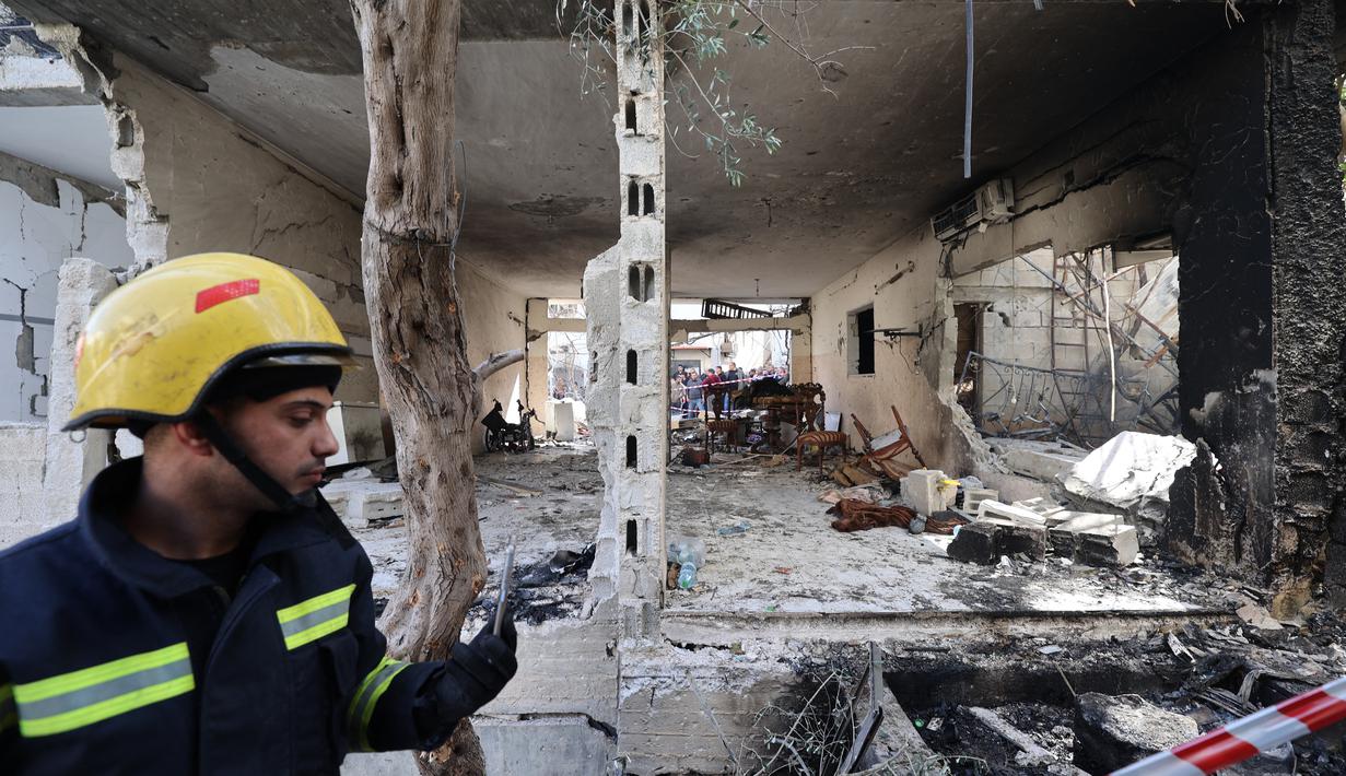 Petugas berada di depan sebuah bangunan yang rusak dan dibakar oleh pasukan Israel selama penggerebekan di kamp pengungsi Jenin Tepi Barat, pada 26 Januari 2023. Tentara Israel menggunakan gas air mata di dalam rumah sakit dan menolak berkomentar ketika ditanya oleh AFP tentang tuduhan gas air mata. (AFP/Jaafar Ashtiyeh)