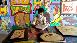 Arfan (55) menyelesaikan karya seni lukis bakar di galeri Rumah Oenik, Kampung Ragamukti, Tajur Halang, Bogor, Senin (28/9/2020). Arfan menjual karya seni lukis bakarnya dengan harga 300 ribu sampai jutaan rupiah dilihat dari besar dan tingkat kerumitannya. (merdeka.com/Arie Basuki)