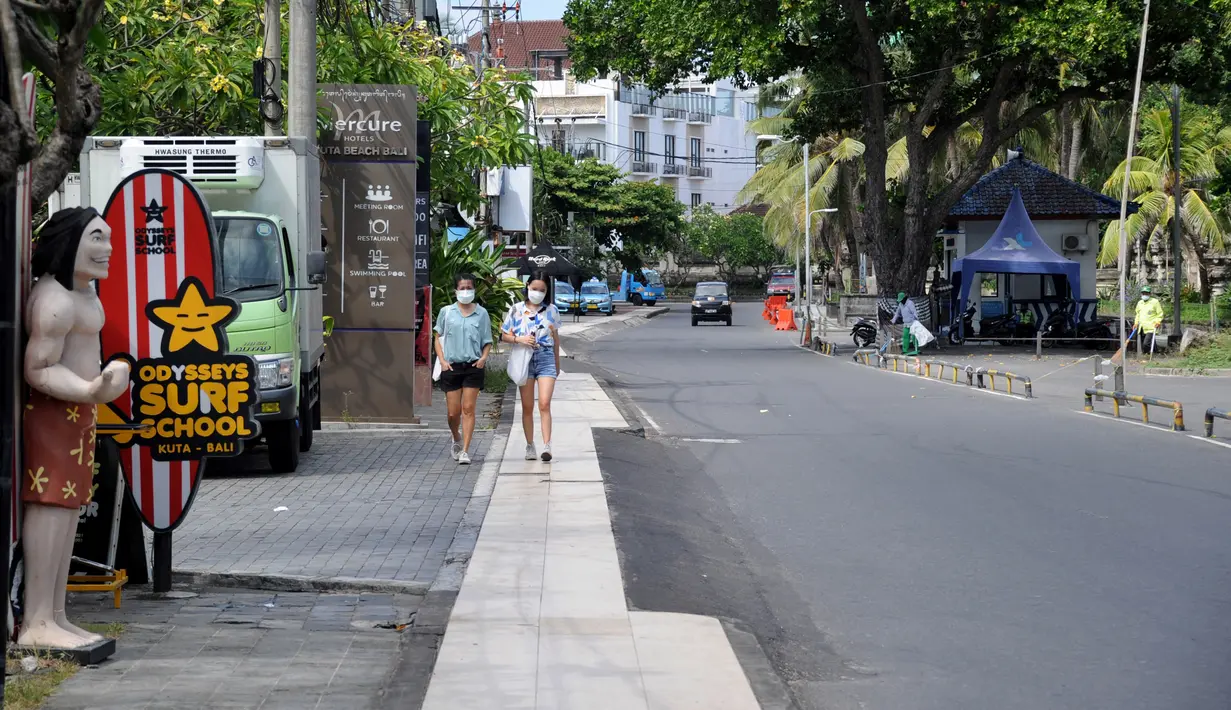 Pejalan kaki berjalan di sepanjang jalan utama yang sepi saat Pemberlakuan Pembatasan Kegiatan Masyarakat (PPKM) Level 3 di Kuta, Badung, Bali, Jumat (23/7/2021). Pemprov Bali tengah menerapkan PPKM Level 3. (SONNY TUMBELAKA/AFP)
