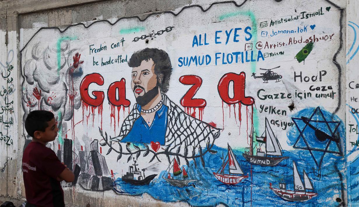 Seorang anak laki-laki Palestina melihat mural yang menggambarkan pencegatan kapal-kapal yang berpartisipasi dalam Armada Sumud Global, sebuah misi bantuan kemanusiaan yang dipimpin sipil ke Gaza melalui laut, di Nuseirat, Jalur Gaza Tengah pada 19 Mei 2026. (Eyad Baba/AFP)