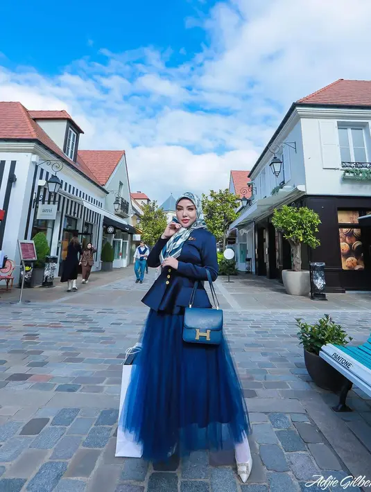 Bella Shofie bergaya princess mengenakan atasan lengan panjang biru navy berbahan satin dengan rok tutu panjang bernuansa senada. Bella Shofie menyempurnakan penampilannya di sini dengan hijab berwarna dasar putih dan bercorak biru serasi, serta tas Hermesnya. [Foto: Instagram/bellashofie_rigan]