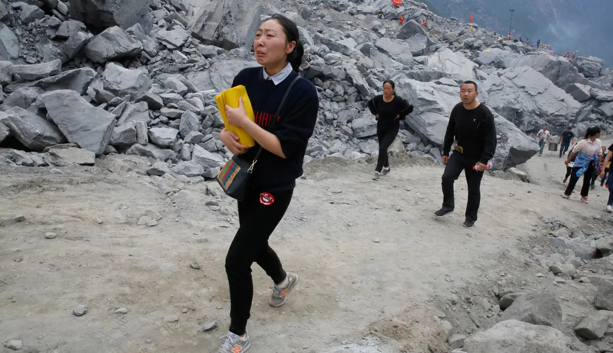 Keluarga menangis sambil membawa kertas ritual untuk menenangkan arwah orang yang tewas di lokasi tanah longsor di desa Xinmo, Sichuan, China (25/6). Sejauh ini, 15 orang telah ditemukan tewas dan puluhan rumah roboh. (AP Photo / Ng Han Guan)