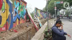 Seorang pria duduk di dekat tembok Jalan Juanda yang ambruk di kawasan Depok, Jawa Barat, Senin (2/12/2019). Kondisi tembok yang dipenuhi mural tersebut mulai rapuh dan sebagian sisinya telah ambruk serta miring sehingga membahayakan pejalan kaki. (Liputan6.com/Immanuel Antonius)