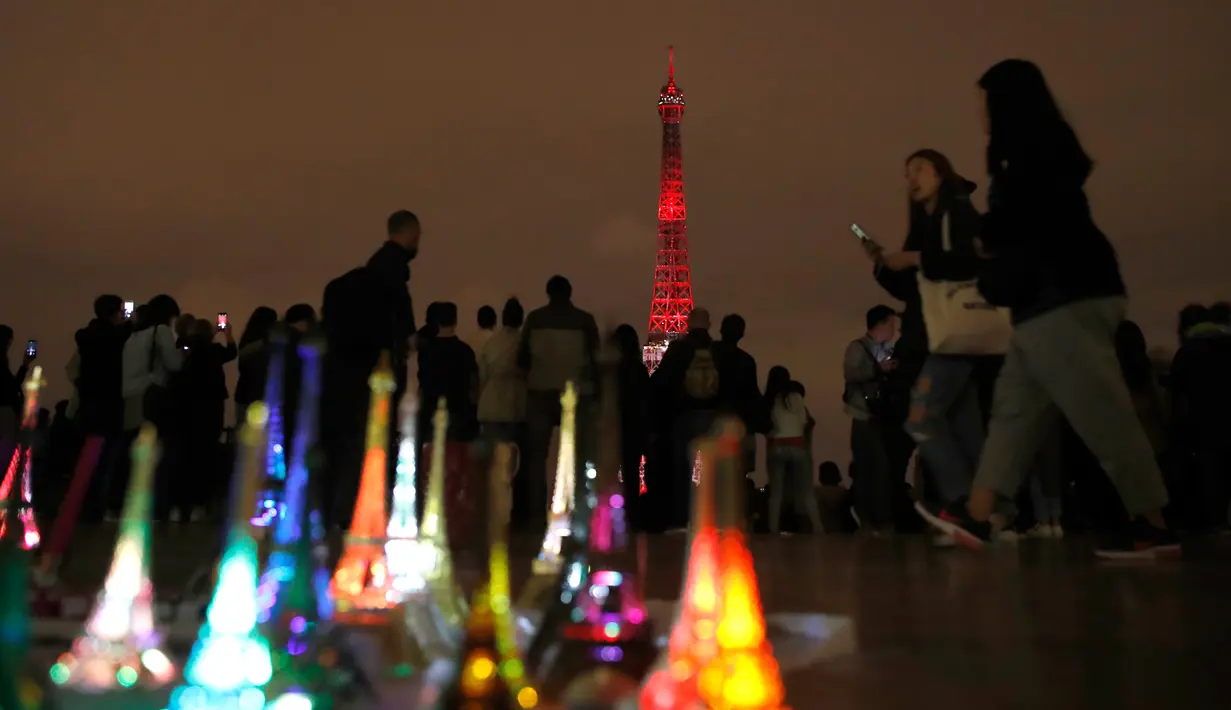 Wisatawan berjalan melewati replika Menara Eiffel yang dijual saat pertunjukan instalasi cahaya di Paris, Perancis, Kamis (13/9). Pertunjukan ini bagian dari kunjungan Putra Mahkota Jepang, Naruhito. (AP Photo/Christophe Ena)