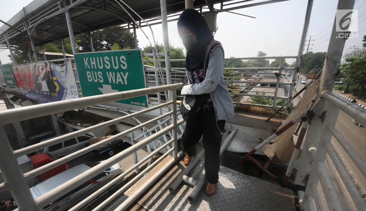 Pejalan kaki melewati lubang di atas JPO di Halte Bus Transjakarta di Jembatan Gantung, Cengkareng, Jakarta, Jumat (27/7). JPO yang rusak akibat tertabrak truk sejak setahun lalu hingga kini belum diperbaiki.  (Liputan6.com/Arya Manggala)
