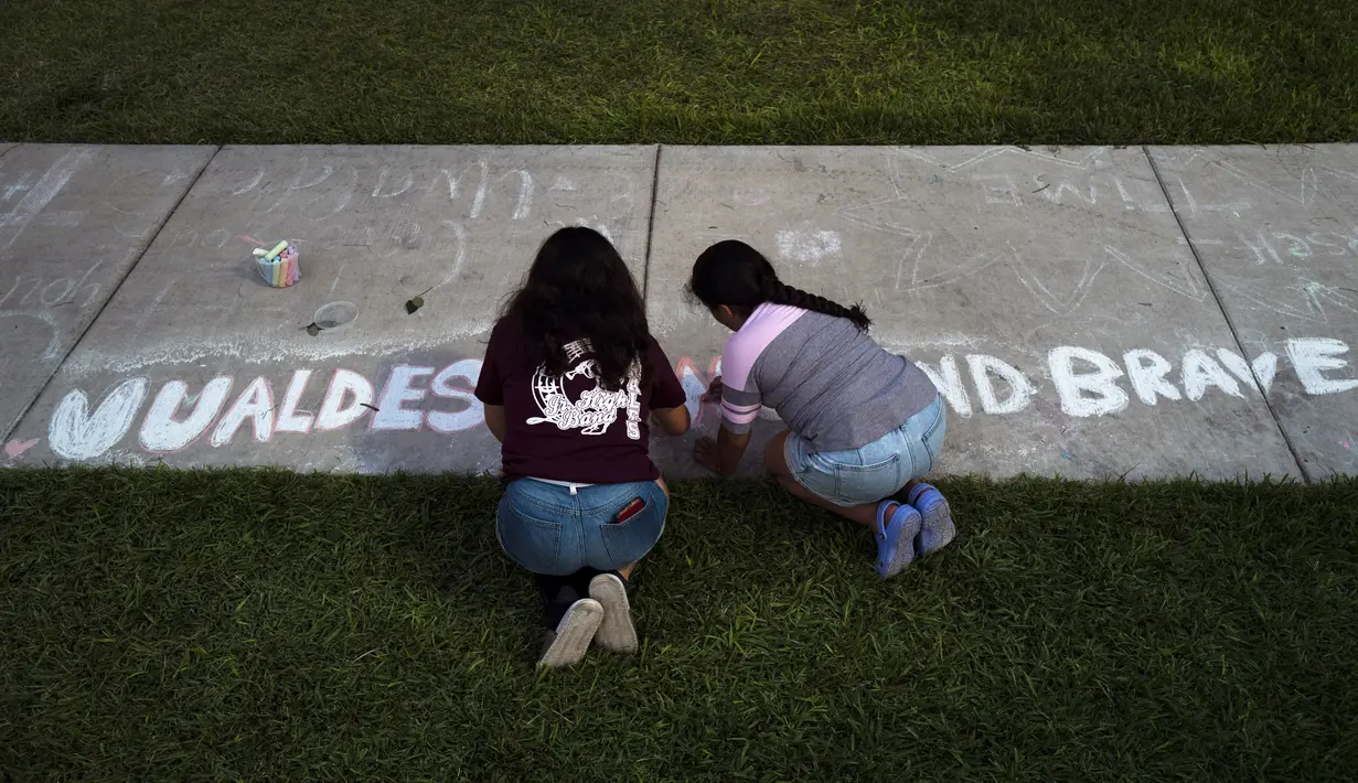 Dua gadis menulis kata-kata penyemangat di jalan setapak di alun-alun kota di mana sebuah peringatan didirikan untuk para korban yang tewas dalam penembakan di sekolah dasar awal pekan ini di Uvalde, Texas, Amerika Serikat, 28 Mei 2022. (AP Photo/Jae C.Hong)