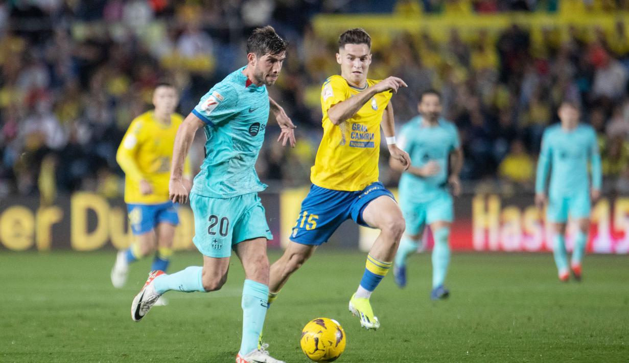 Pemain Barcelona, Sergi Roberto, berusaha melewati pemain Las Palmas, Mika Marmol, pada laga La Liga 2023/2024 jornada 19 di Estadio de Gran Canaria, Jumat (5/1/2024). Barca sejatinya sempat tertinggal lebih dahulu akibat gol Munir El Haddadi. Pasukan Xavi bangkit dengan mencetak gol lewat aksi Ferran Torres di awal babak kedua dan eksekusi penalti Ilkay Gundogan di masa injury time. (AFP/Desiree Martin)