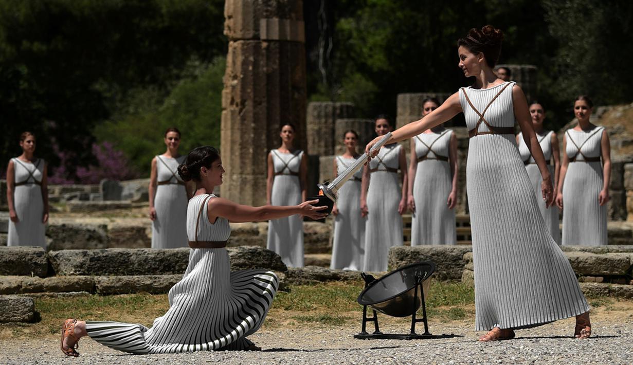 Aktris Yunani, Katerina Lechou, memberikan api olimpiade yang baru saja dinyalakan dalam suatu upacara di Candi Hera yang terletak di bekas kota tua Olympia, Yunani, Kamis (21/4/2016). (AFP/Aris Messinis)