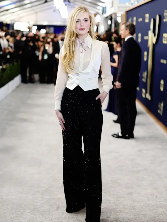 Elle Fanning memilih tampil memukau dengan business suit dari Gucci di red carpet SAG Awards, lengkap dengan blouse krem, rompi putih, celana hitam berkilau, perhiasan dari Cartier, dan cincin dari Pasquale Bruni.