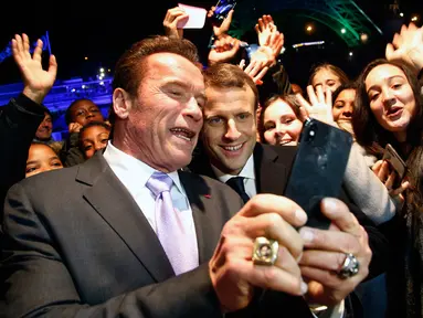 Aktor yang juga mantan Gubernur California, Arnold Schwarzenegger berswafoto dengan Presiden Prancis, Emmanuel Macron (tengah) berlatar belakang Menara Eiffel seusai menghadiri KTT One Planet Summit di Paris, Selasa (12/12). (AP/Thibault Camus, Pool)