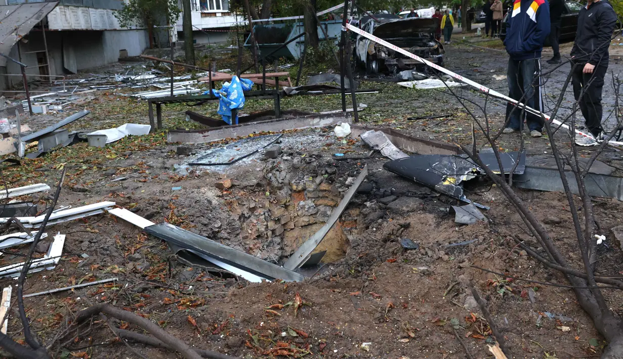 Serangan rudal Rusia juga menghantam wilayah lain di Ukraina, seperti Zaporizhzhia. Tampak dalam foto, beberapa warga berdiri di dekat kawah di depan sebuah rumah yang hancur akibat serangan Rusia di Zaporizhzhia, Ukraina, Minggu 5 Oktober 2025. (AP Photo/Kateryna Klochko)