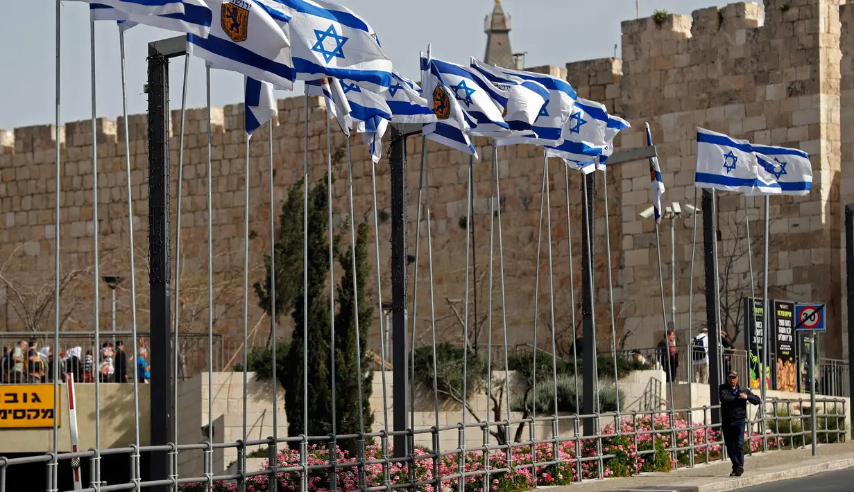 Seorang pria berjalan di bawah bendera Israel di dekat Gerbang Jaffa di Kota Tua Yerusalem (20/3). (AFP Photo/Thomas Coex)