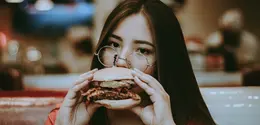 Ilustrasi perempuan makan burger/copyright unsplash.com/Hector Gomez