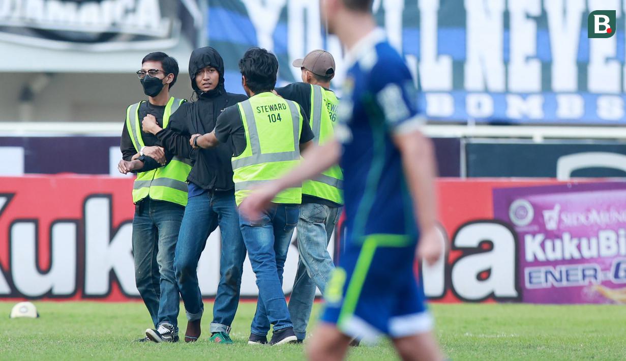<p>Petugas keamanan menangkap suporter yang masuk ke lapangan saat Persib Bandung melawan Persik Kediri pada laga BRI Liga 1 2022/2023 di Stadion Pakansari, Bogor, Rabu (8/3/2023). (Bola.com/M Iqbal Ichsan)</p>
