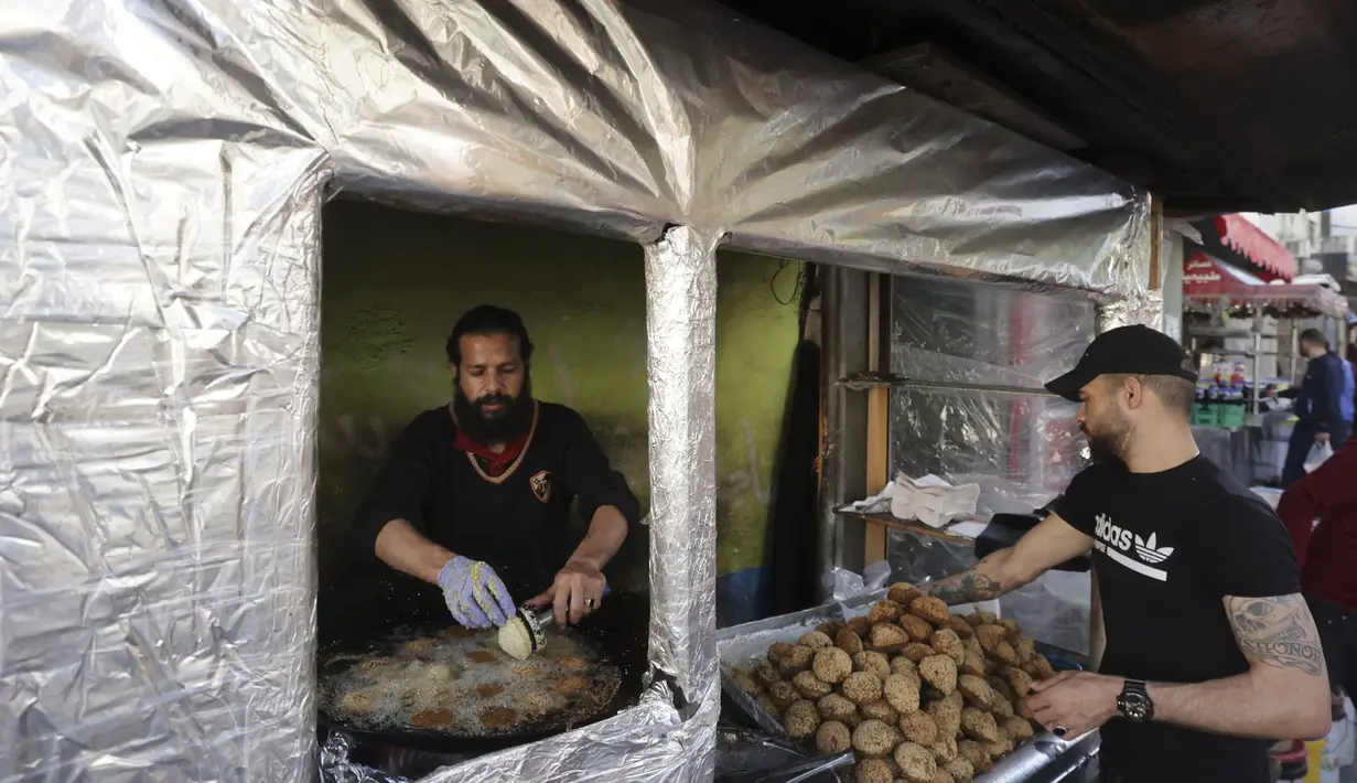 Warga Palestina membuat falafel, makanan yang disukai untuk berbuka puasa, selama bulan suci Ramadhan di pusat kota Hebron di Tepi Barat yang diduduki (9/4/2022). Makanan ini dibuat dari kacang Arab yang digiling dan kemudian dipadatkan dan dibuat bola-bola kecil lalu digoreng. (AFP/Hazem Bader)