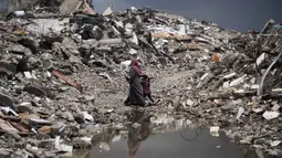 Diketahui, sebagian besar warga masih menempati tenda-tenda dan tempat penampungan sementara lainnya setelah perang antara Israel dan Hamas sejak Oktober 2023 silam. Tampak dalam foto, warga Palestina berjalan melewati reruntuhan di tengah cuaca buruk Kota Gaza, Kamis 11 Desember 2025. (AP Photo/Jehad Alshrafi)