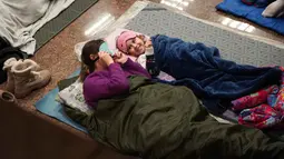Saat terjadi serangan Rusia, ribuan warga Kyiv, termasuk ratusan anak-anak, berlindung di peron stasiun metro. Tampak dalam foto, seorang wanita dan seorang anak berlindung di stasiun metro selama serangan udara Rusia di Kyiv, pada Selasa 3 Februari 2026 pagi waktu setempat. (Serhii Okunev/AFP)