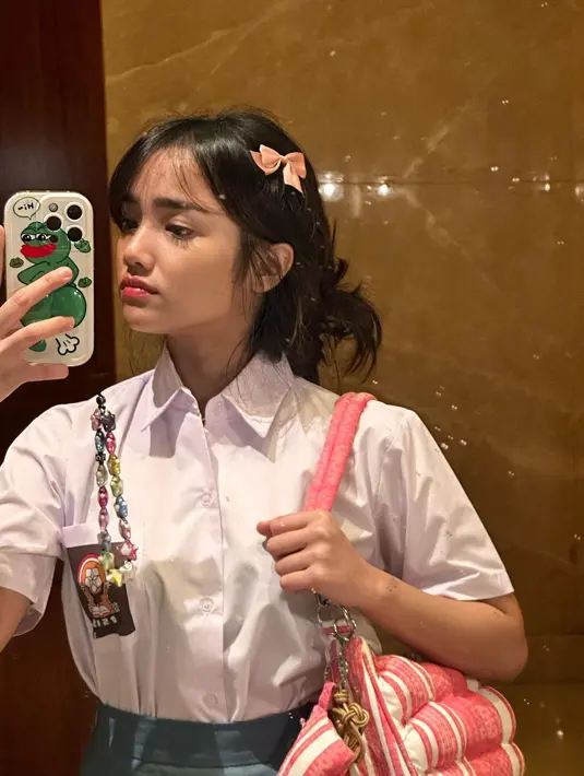 Fuji terlihat menenteng shoulder bag model kasur kapuk. Tas warna merah muda itu dipermanis dengan gantungan yang juga memiliki model bak sapu kasur.