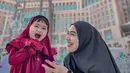 Ria Ricis berpose bersama Moana saat Umroh. Ricis yang memilih tampilan serba hitam tampak berpose tertawa menggemaskan di samping sang putri Moana, yang memilih tampilan serba merah. [Foto: Instagram/riaricis1795]