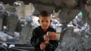 Sejak dimulainya gencatan senjata yang rapuh itu, sedikitnya 280 warga Palestina tewas dan lebih dari 670 orang luka-luka akibat serangan Israel. Sementara laporan sebelumnya dari otoritas kesehatan Gaza, terdapat hampir 70.000 orang tewas sejak konflik pecah dua tahun lalu. Tampak dalam foto, seorang anak laki-laki Palestina memegang barang-barangnya di tengah puing-puing bangunan yang rusak milik Kementerian Wakaf Agama, yang menjadi tempat penampungan bagi pengungsi di kawasan Zeitoun, Kota Gaza, pada Kamis 20 November 2025, sehari setelah bangunan tersebut menjadi sasaran serangan militer Israel. (Omar AL-QATTAA /AFP)