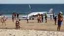 Sejumlah orang berjalan melewati sebuah pesawat kecil yang melakukan pendaratan darurat di pantai Sao Joao yang ramai dekat Lisbon, Portugal, Rabu (2/8). Akibatnya, pesawat itu melindas dua pengunjung pantai yang sedang berjemur. (AP Photo/Armando Franca)