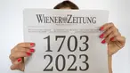 Seorang wanita memegang koran "Wiener Zeitung" terbitan 27 April 2023 dengan halaman depan yang menggambarkan usia surat kabar tersebut selama 320 tahun di Wina, Austria, 27 April 2023. Wiener Zeitung adalah salah satu surat kabar tertua di dunia. (JOE KLAMAR/AFP)