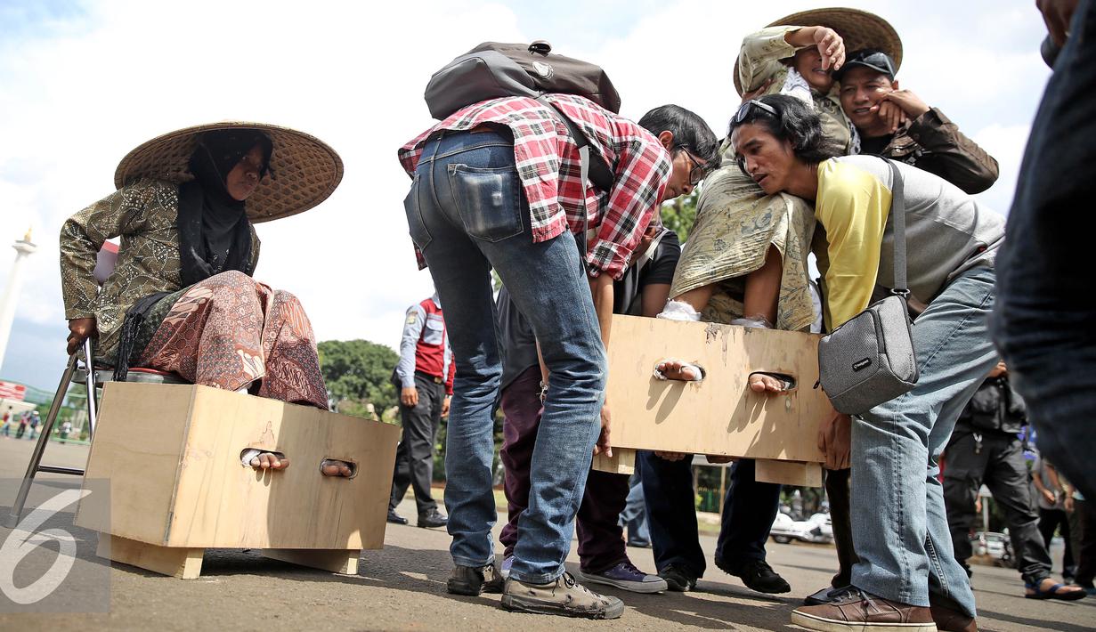 Petani perempuan yang disemen kakinya diangkat saat aksi mengecor kakinya di depan Istana Negara, Jakarta, Selasa (13/4). Aksi tersebut sebagai penolakan terhadap tambang dan pabrik semen di Pegunungan Kendeng, Jateng. (Liputan6.com/Faizal Fanani)