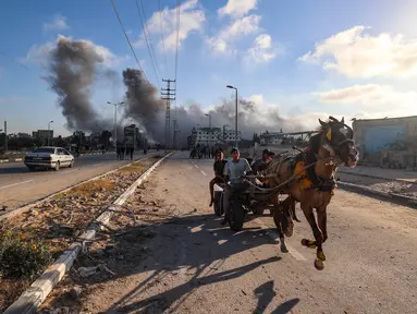 Gumpalan asap hitam membumbung tinggi selama serangan Israel ketika warga Palestina yang mengendarai gerobak yang ditarik kuda melaju di sepanjang jalan Salah al-Din di dekat kamp pengungsi Nusseirat, Jalur Gaza Tengah, pada 25 Juni 2025. (Eyad BABA/AFP)