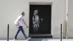 Seorang pria berjalan melewati mural yang diduga karya seniman sekaligus aktivis Banksy di Paris, Prancis, Minggu (24/6). Seniman jalanan misterius asal Inggris itu membuat mural bertema migrasi. (THOMAS SAMSON/AFP)