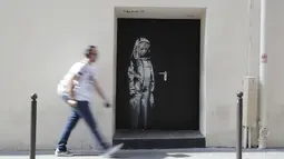 Seorang pria berjalan melewati mural yang diduga karya seniman sekaligus aktivis Banksy di Paris, Prancis, Minggu (24/6). Seniman jalanan misterius asal Inggris itu membuat mural bertema migrasi. (THOMAS SAMSON/AFP)